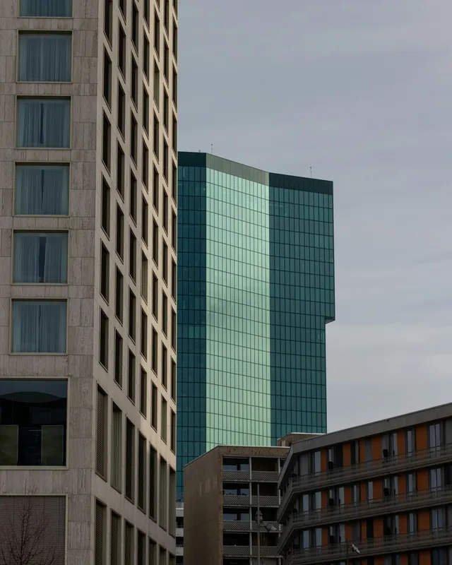 Tall stone-clad and glass towers rising above neighbouring buildings under a grey sky.