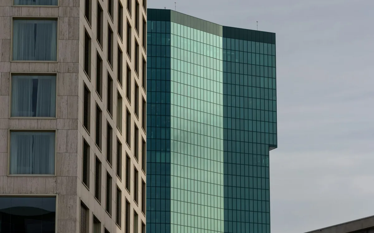 Tall stone-clad and glass towers rising above neighbouring buildings under a grey sky.
