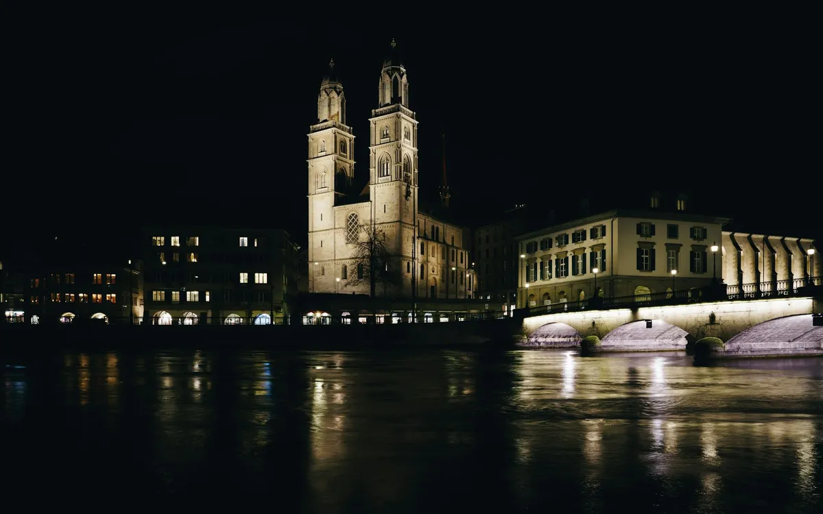 The twin towers of the Grossmünster and a floodlit bridge, seen across the Limmat at night.