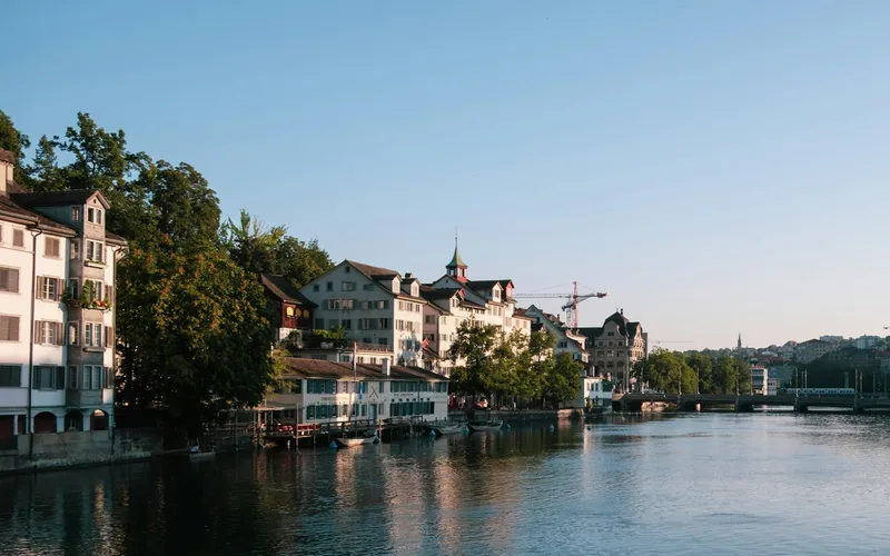 Houses along the Limmat in low evening light, with a bridge in the distance.