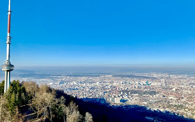 A broadcast mast on a hillside above a wide view over the city of Zurich on a clear day.